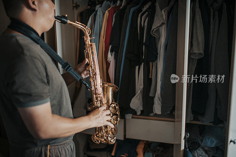 asian chinese mid adult man practicing saxophone facing his wardrobe as soundproof to reduce the sounds disturbing his neighbor  in his apartment